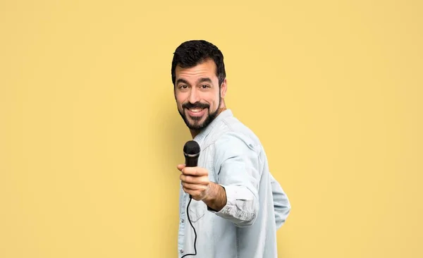 一个留着胡子的英俊男人 带着话筒在孤零零的黄色背景上歌唱 — 图库照片