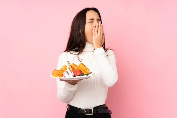 若いですブルネット女性保持Waffles上の隔離されたピンクの背景Yawningとカバー広いオープン口とともに手 — ストック写真