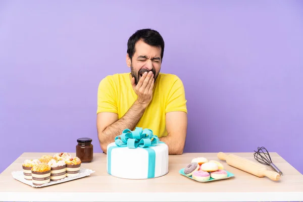 Man in a table with a big cake yawning