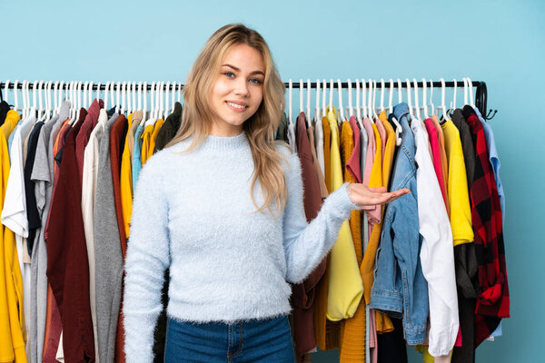 Teenager Russian girl buying some clothes isolated on blue background presenting an idea while looking smiling towards