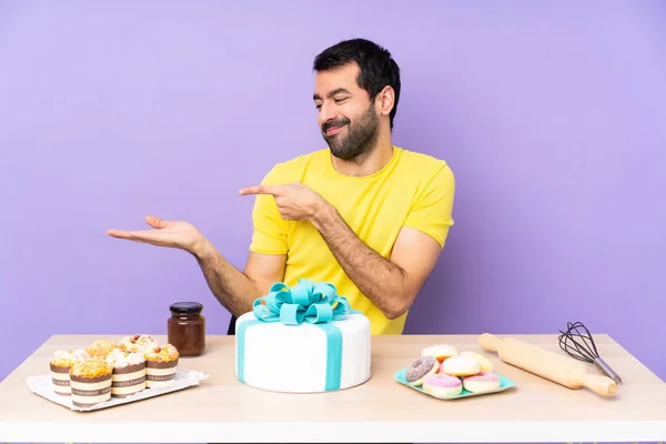 Man in a table with a big cake holding copyspace imaginary on the palm to insert an ad