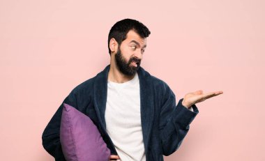 Pijamalı sakallı bir adam, kopyasal alan tutuyor ve pembe arka plan hakkında şüpheleri var.