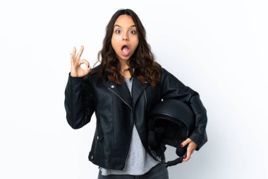 İzole edilmiş beyaz arka plan üzerinde motosiklet kaskı tutan genç bir kadın şaşırdı ve iyi işareti gösteriyor.