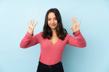 Mavi arka planda izole edilmiş genç melez kadın parmaklarıyla dokuzu sayıyor.