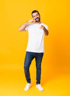 Sarı arka planda sakallı, telefon hareketleriyle ön tarafı işaret eden uzun boylu bir adam resmi.