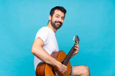 Mavi arka planda gitar çalan genç bir adam.