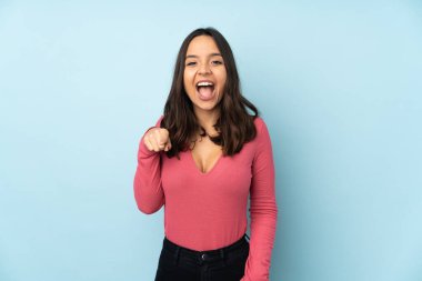 Genç melez kadın mavi arka planda izole edilmiş şaşırmış ve ön tarafı işaret ediyor.