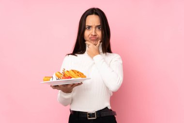 Genç esmer kadın, izole edilmiş pembe arka planda waffle tutuyor.