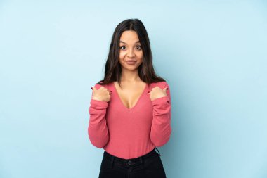 Mavi arka planda, şaşırtıcı bir yüz ifadesi olan genç melez bir kadın.