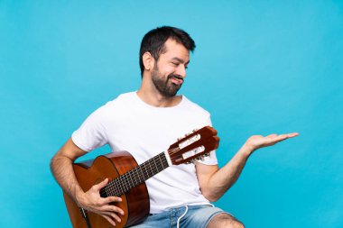 İzole edilmiş mavi arka planda gitarı olan genç bir adam, telif alanını şüpheyle tutuyor