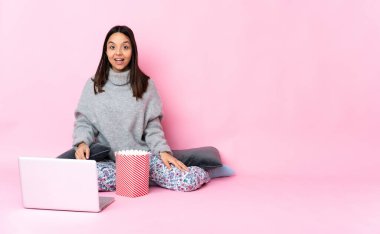 Genç melez bir kadın laptopta film izlerken patlamış mısır yiyor ve yüzünde sürpriz bir ifade var.