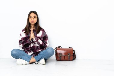 Yerde oturan genç bayan öğrenci avuç içlerini bir arada tutuyor. İnsan bir şey ister.