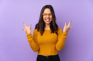 Mor arka planda izole edilmiş genç melez kadın kaya jesti yapıyor.