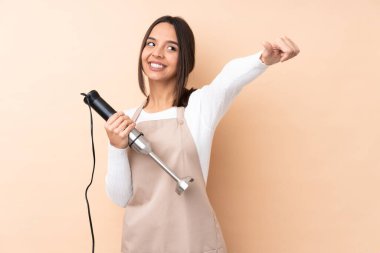 Genç esmer kız, el blendırını izole edilmiş arka planda kullanıyor. Baş parmak hareketi yapıyor.