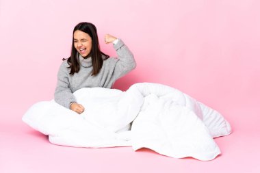 Genç melez kadın pijama giymiş yerde oturmuş zaferi kutluyor.