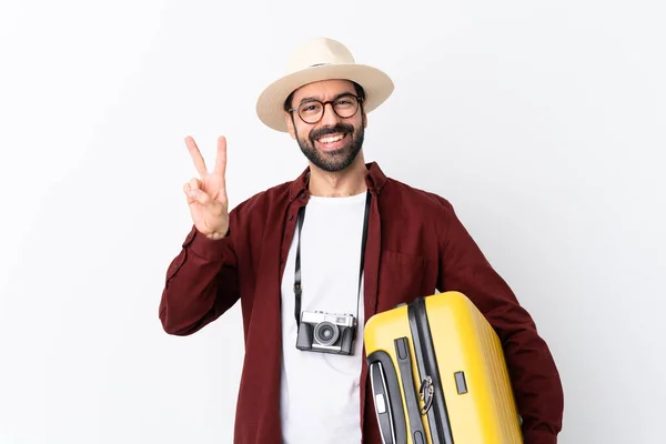 Traveler man man with beard holding a suitcase over isolated white background showing victory sign with both hands