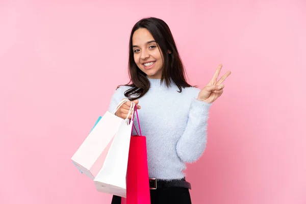 若いです女性とともにショッピングバッグ以上隔離されたピンクの背景ショー勝利サインとともに両手 — ストック写真