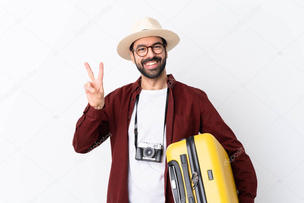 Traveler man man with beard holding a suitcase over isolated white background showing victory sign with both hands