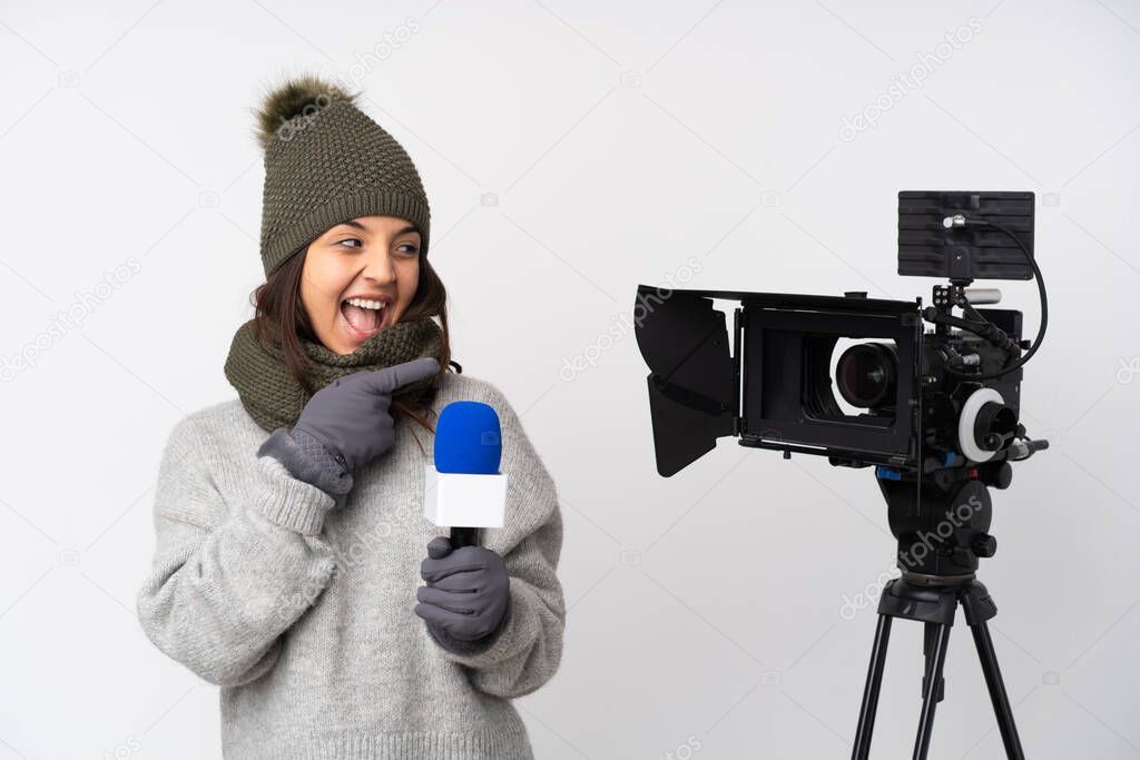 Reporter woman holding a microphone and reporting news over isolated white background pointing finger to the side and presenting a product