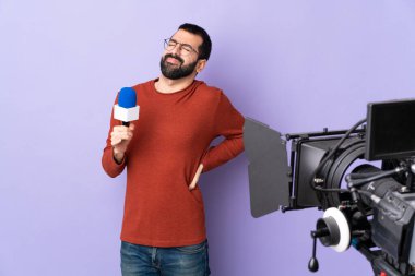 Elinde mikrofon tutan muhabir, gayret gösterdiği için sırt ağrısı çeken izole edilmiş mor bir arka planda haber sunuyor.