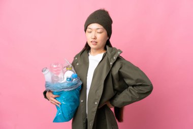 Bir çanta dolusu plastik şişeyi elinde tutan Çinli bir kız izole edilmiş pembe arka plan üzerinde geri dönüşüm yapmak için çaba sarf ettiği için sırt ağrısı çekiyor.