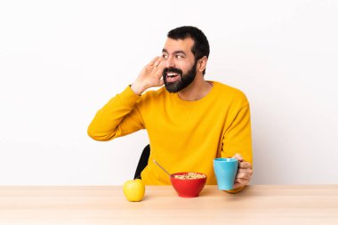 Kafkasyalı bir adam bir masada kahvaltı yapıyor. Kulağına elini sürerek bir şeyler dinliyor..