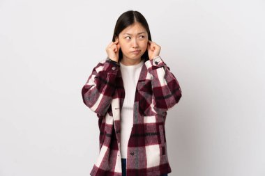 Genç Çinli kız izole edilmiş beyaz arka planda hayal kırıklığına uğramış ve kulaklarını kapatmış.