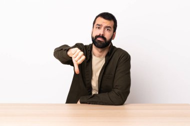 Masada sakallı beyaz bir adam, olumsuz bir ifadeyle baş parmağını aşağı gösteriyor..