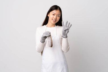 Çinli balıkçı önlük takıyor ve soyutlanmış beyaz arka planda çiğ balık tutuyor mutlu ve parmaklarıyla dört tane sayıyor.