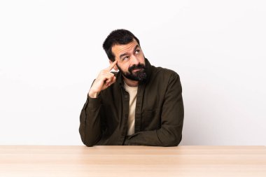 Masada sakallı, beyaz bir adam. Çılgınlık jesti yapıyor. Parmağını kafaya koyuyor..