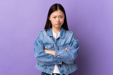 Genç Çinli kız, mutsuz bir ifadeyle izole edilmiş mor arka plan.