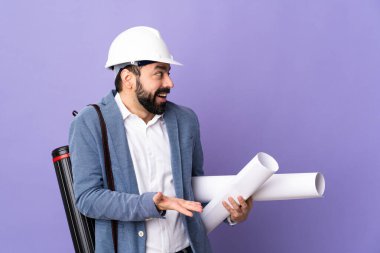 Miğferli genç bir mimar, elinde yalıtılmış mor bir arkaplan, sürpriz bir ifadeyle yan yana bakıyor.