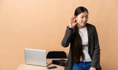 İşyerindeki Çinli iş kadını elini kulağına koyarak bir şeyler dinliyor.