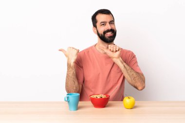 Beyaz bir adam bir masada kahvaltı yapıyor. Ürünü sunmak için yan tarafı işaret ediyor..
