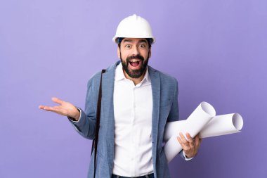 Miğferli genç bir mimar. Yüzünde şok ifadesi olan, izole edilmiş mor bir arkaplan üzerinde planlar tutuyor.