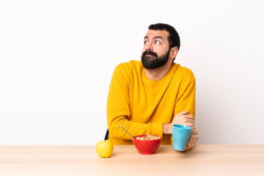 Masada kahvaltı yapan beyaz bir adam omuzlarını kaldırırken şüpheyle hareket ediyor..