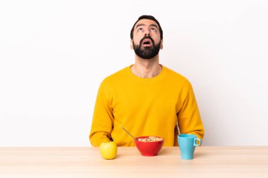 Masada kahvaltı yapan beyaz bir adam yukarı bakıyor ve şaşırmış bir ifadeyle.