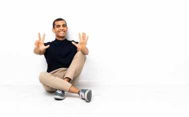 Afro-Amerikalı adam yerde oturmuş parmaklarıyla sekizi sayıyor.