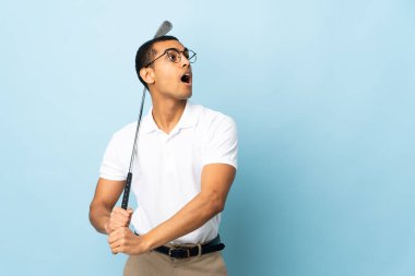 İzole edilmiş mavi arka planda golf oynayan Afrikalı Amerikalı bir adam.