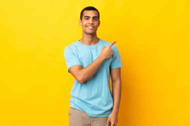 İzole edilmiş arka planda yaşayan Afrikalı Amerikalı bir adam bir ürünü sunmak için kenarı işaret ediyor.