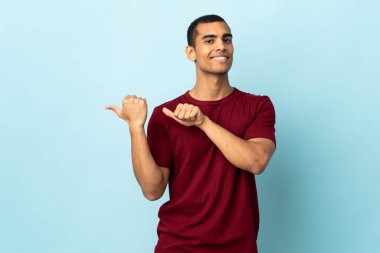 İzole edilmiş arka planda yaşayan Afrikalı Amerikalı bir adam bir ürünü sunmak için kenarı işaret ediyor.