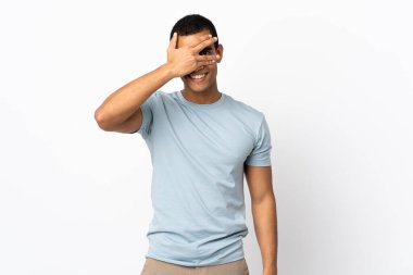 İzole edilmiş beyaz arka plan üzerinde Afrika kökenli Amerikalı bir adam elleriyle gözlerini kapatıyor ve gülümsüyor.