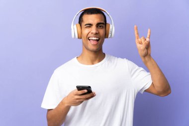 İzole edilmiş mor arka planda gezici bir rock hareketi yaparak müzik dinleyen Afrikalı Amerikalı bir adam.