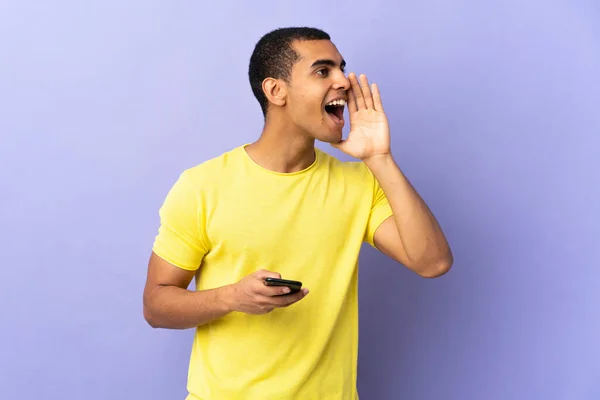 Africký Američan Přes Izolované Fialové Pozadí Pomocí Mobilního Telefonu Křičí — Stock fotografie