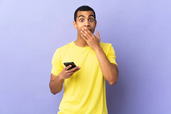 African American Man Isolated Purple Background Using Mobile Phone Surprise — Stock Photo, Image