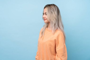 İzole edilmiş mavi arka planda genç bir kız yan tarafa bakıyor.