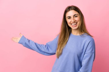 Soyutlanmış pembe arka planda genç bir kadın. Davet edilmek için ellerini yana uzatıyor.