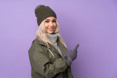 Kışlık şapkalı genç sarışın kız izole edilmiş mor arka planda geriye bakıyor.