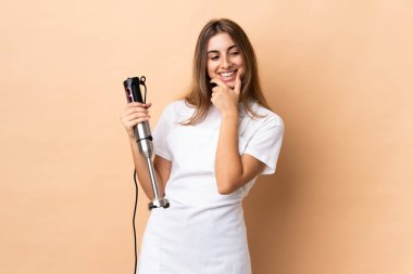 El blenderi kullanan bir kadın izole edilmiş arka planda yan tarafa bakıyor ve gülümsüyor.