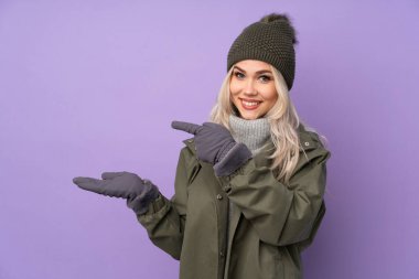 Kışlık şapkalı, mor arka planı olan genç sarışın kız bir ilan vermek için fotokopi makinesini avucunun içinde tutuyor.